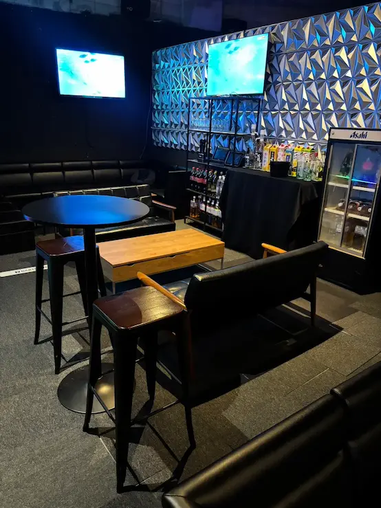 The small lounge seating area inside EVE in Osaka, with low couches, tables, screens, and bottles along the wall