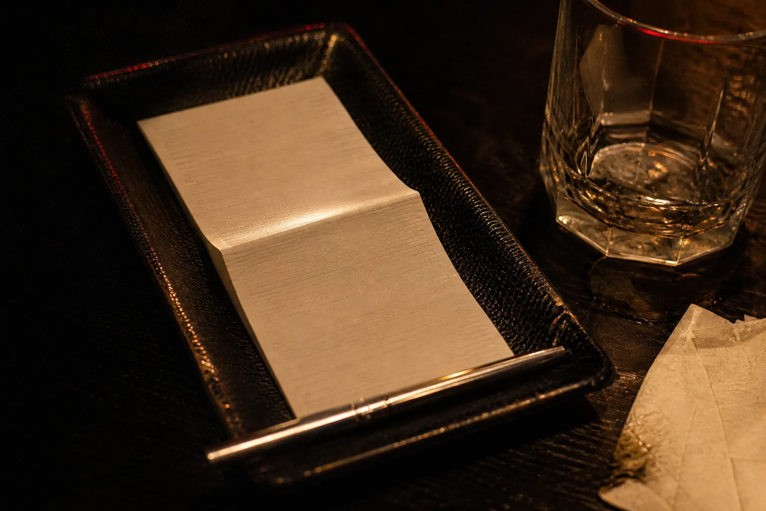An itemised kyabakura bill folded into a leather card tray beside an empty glass on a dark table