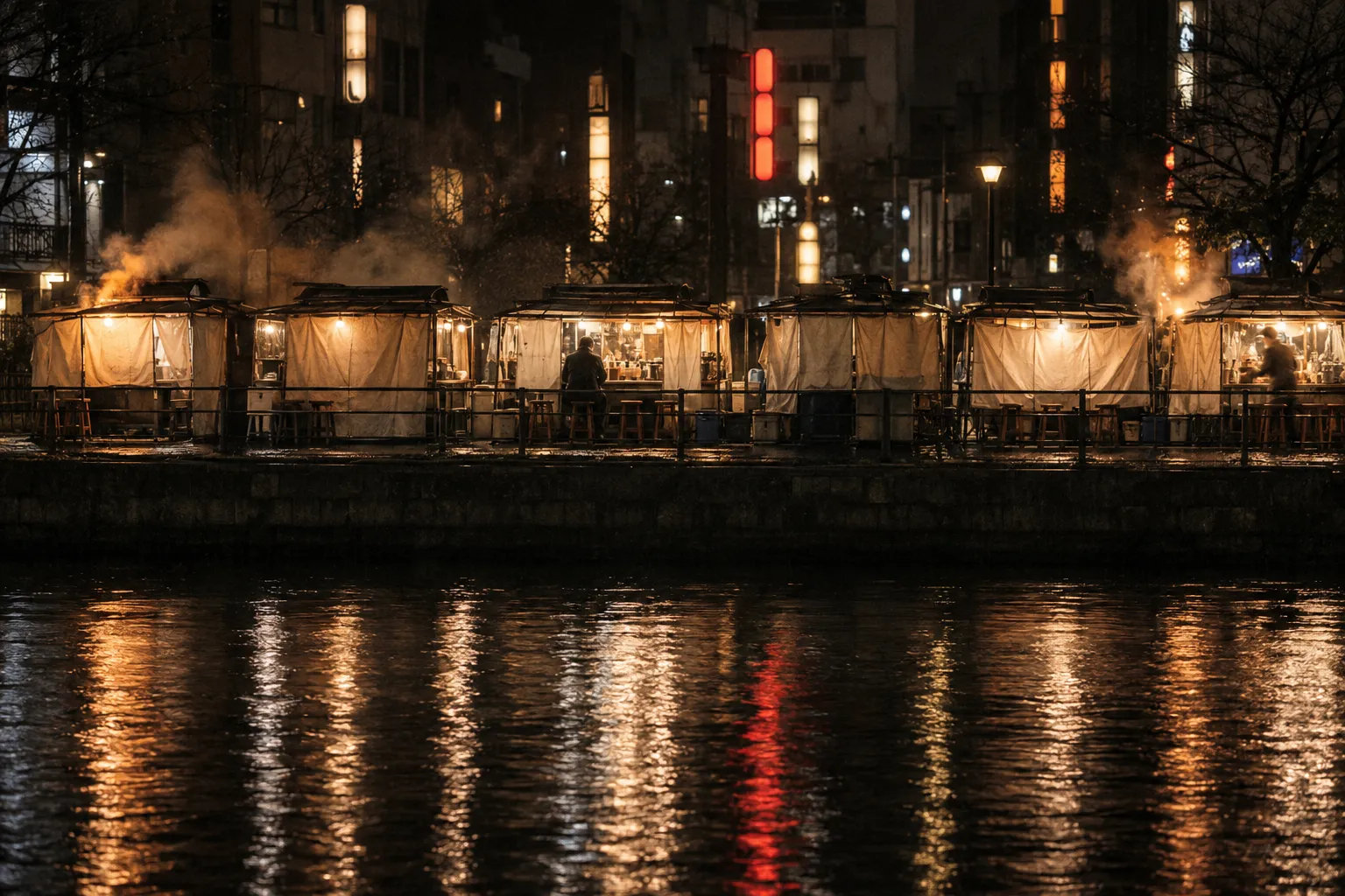 The Nakasu riverside food stall row in Fukuoka at night seen across black water