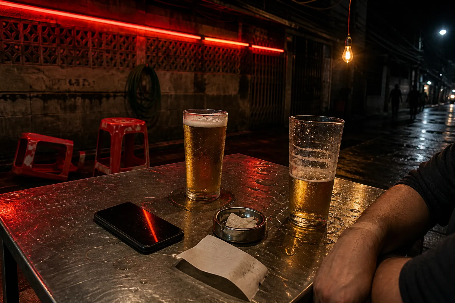 Two beers and a face down phone on a steel table at a Bangkok street bar at night
