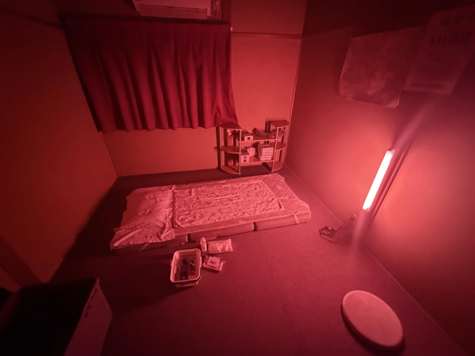 A small private room in Tobita Shinchi lit by red fluorescent tubes, with floor bedding and a low table