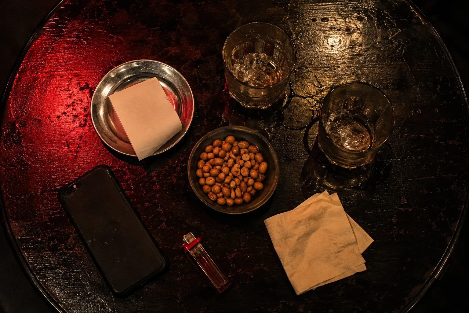 An overhead view of a bar table in Vietnam at night with a folded receipt on a steel tray and two empty glasses